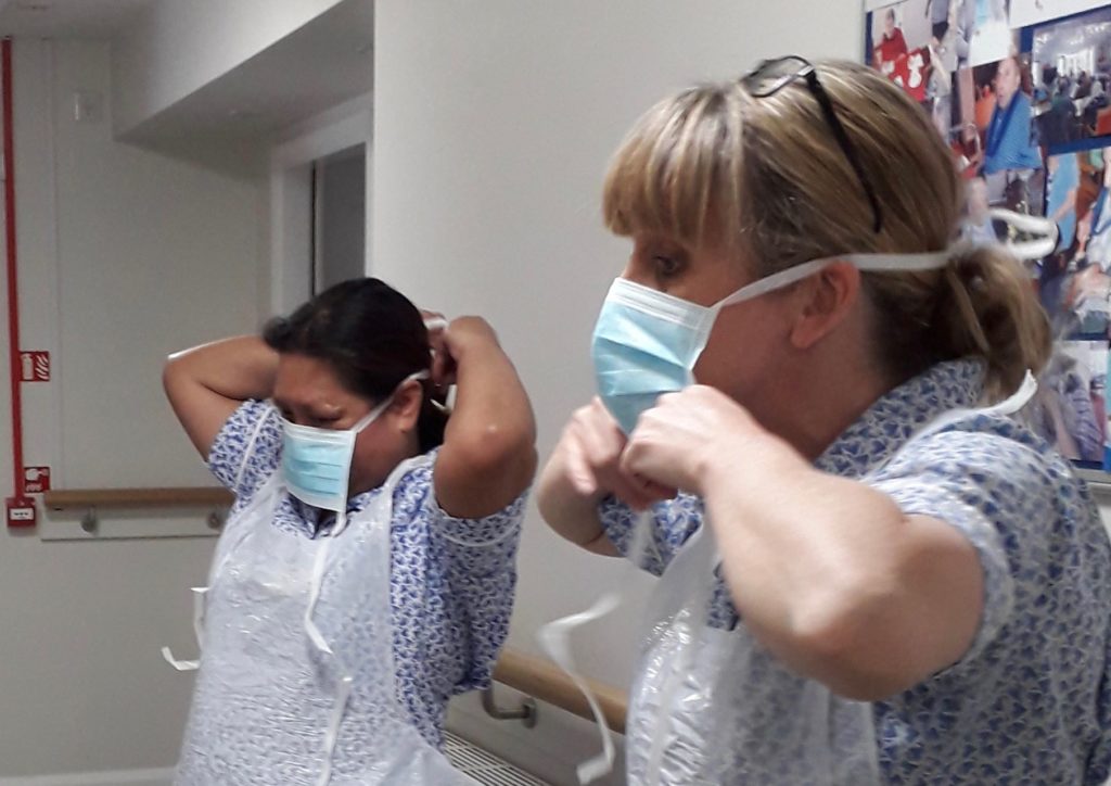 Two care home workers are putting on their PPE masks and aprons