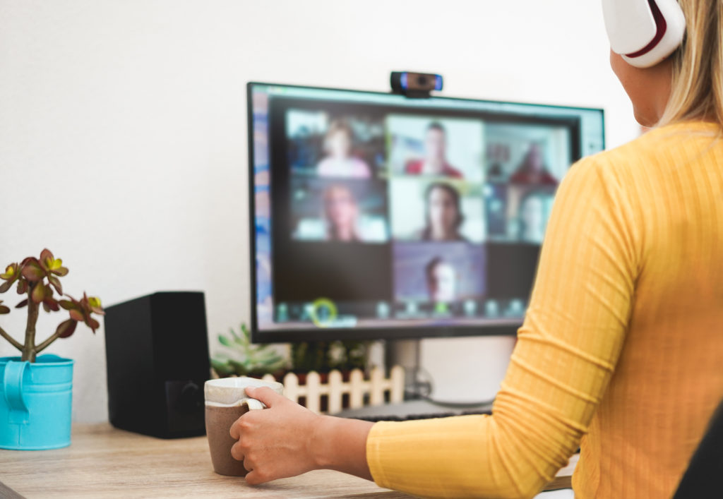 A young woman is wearing headphones and speaking to work colleagues on a computer screen