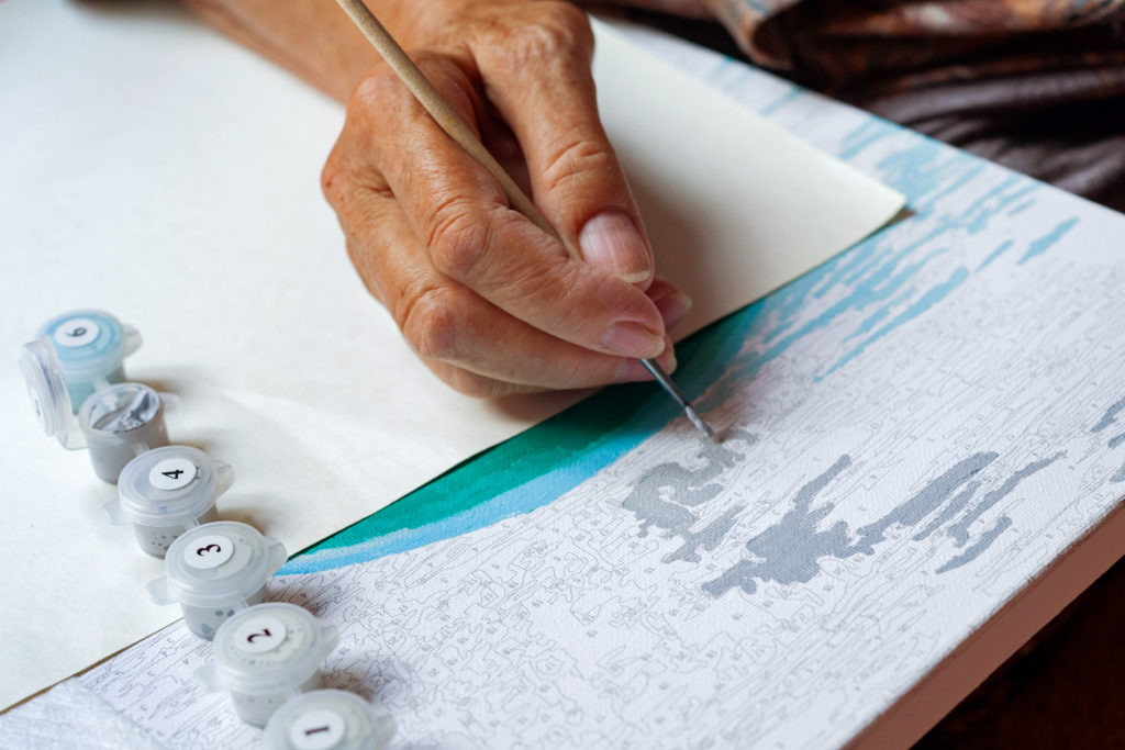 An older person is using a painting by numbers kit