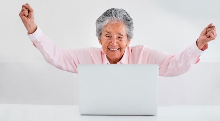 An elderly lady celebrates doing something on her laptop